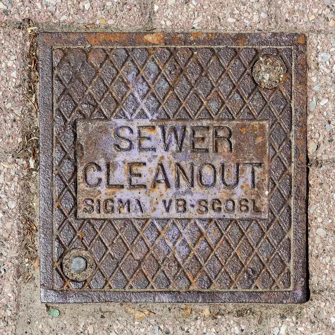 Round cast-iron cover marked Sewer Cleanout