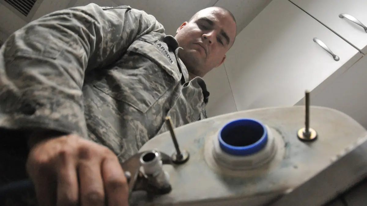 Maintenance worker reaching into an open toilet tank to work on the valve